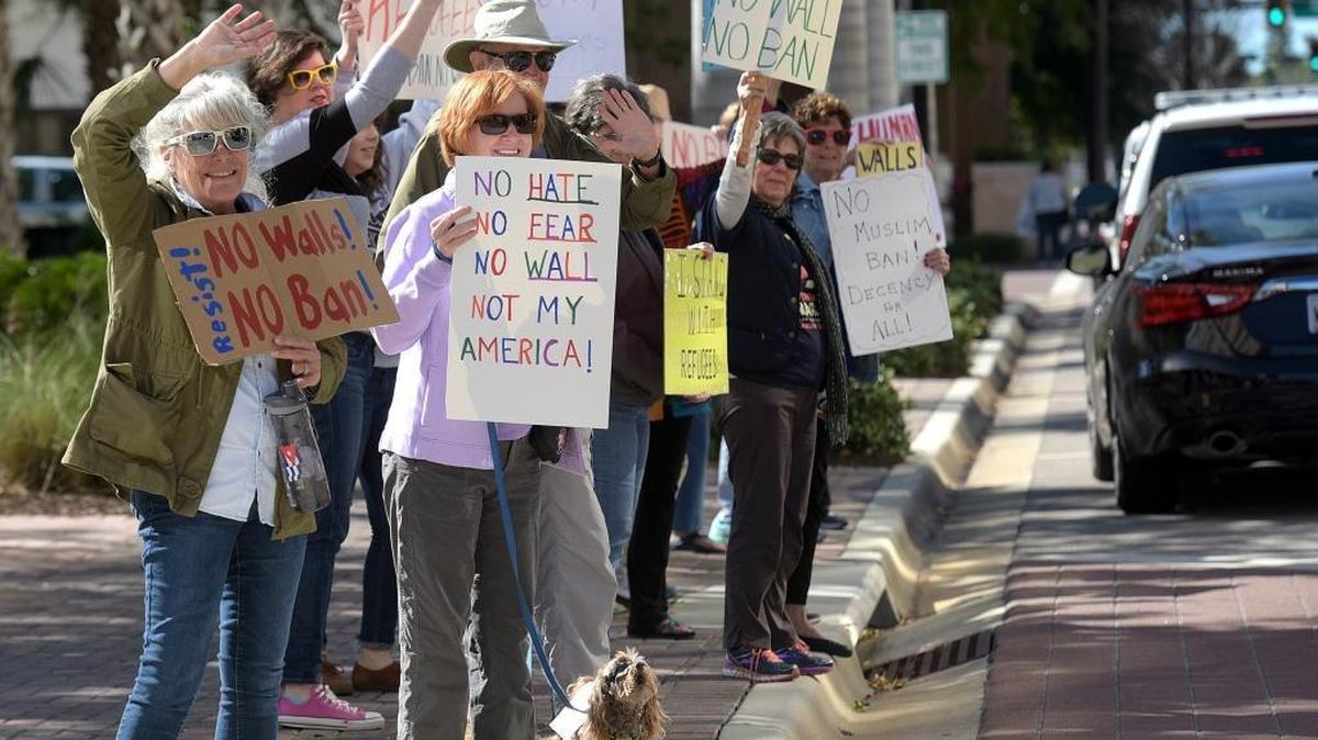 People with signs gather to protest President Donald Trump’s immigration ban in front of Rep. Vern Buchanan’s office Monday afternoon along Manatee Avenue.