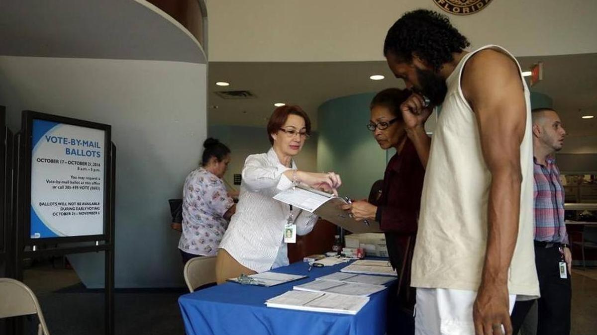 Mayra Rodriguez, left, assists people with a voter registration form at the Miami-Dade County Elections Department, Wednesday, Oct. 12, 2016, in Doral.