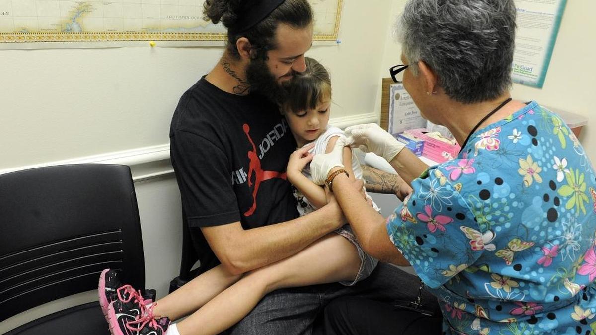 Faith Ann Craven, 5, sits on her father, Justin's lap while she gets a shot from Cathy Joyce, R.N., at the Manatee County Health Department in this file photo from 2013 during a rush to get immunizations before school starts.