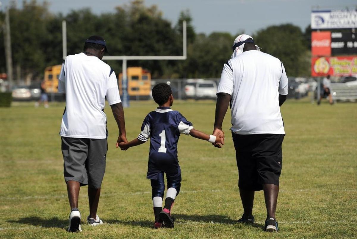 A young tiny-mite football player holds hands with adults as he walks onto the football field at the Palmetto Youth Center in this file photo.