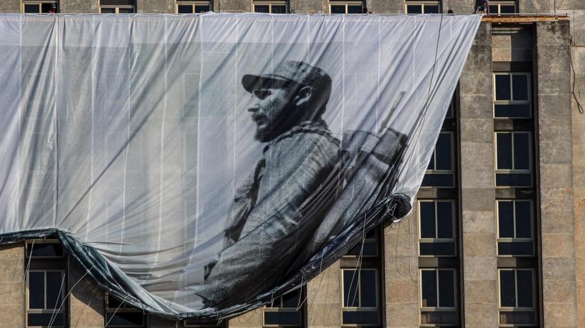 Men hang a giant banner with a picture of Cuba's late leader Fidel Castro as a young revolutionary, from the Cuban National Library building in Havana.