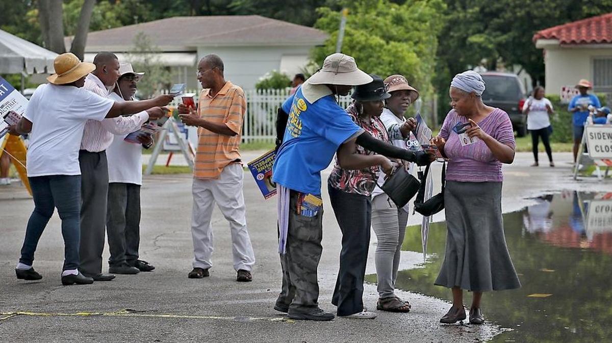 Various campaign workers approach voters as they go to cast their votes at the North Miami Library polling station on Sunday, August 28, 2016.