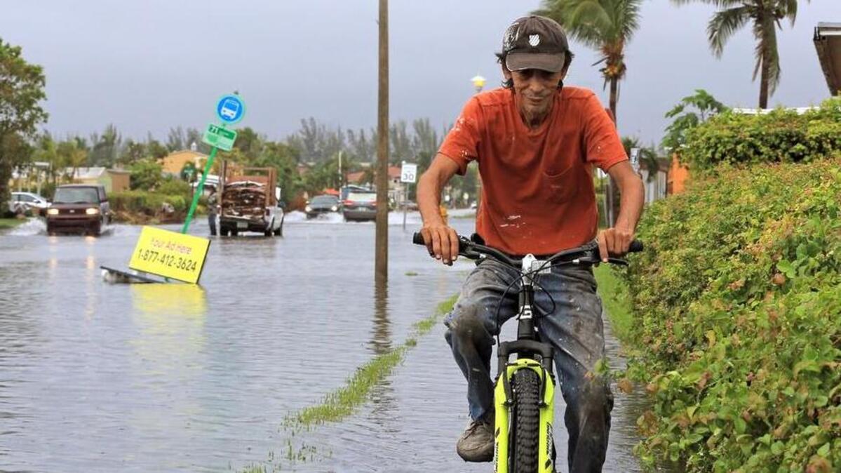 A man bikes through the flooding in Sweetwater in October. Cities that wait to address the effects of climate change, like sea-level rise, could pay more in bonds.