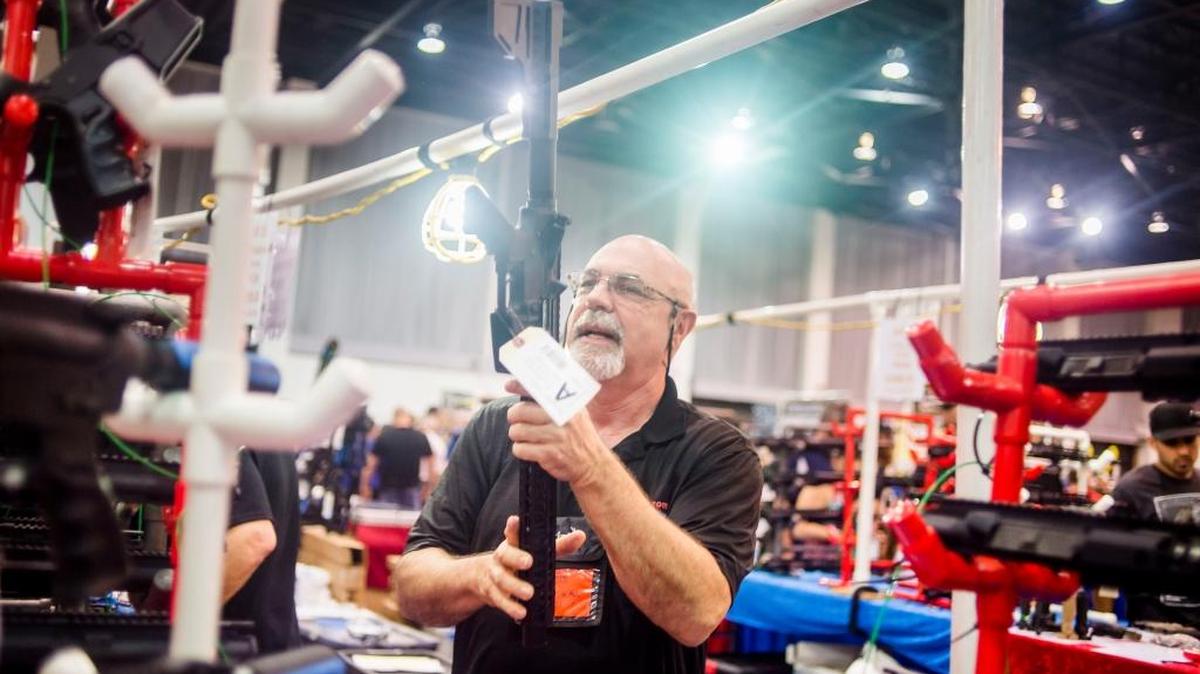 Scott Rollf, of 22 Mods For All, speaks with customers while holding an AR-15 style rifle at the Florida Gun Show in Tampa, Feb. 25, 2018. Many Americans are financially connected to the firearms industry through retirement plans or index funds that own stocks in gun companies.