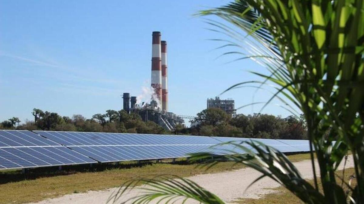 FILE: The FPL Manatee Solar Energy Center’s solar panels in Parrish stand in contrast to smoke stacks where fossil fuel is used to generate electricity.
