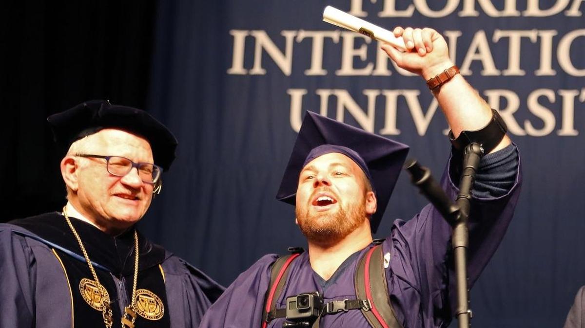 File photo of Florida International University graduate Shane Mosko, center, as he lifts up his diploma as he shakes the hands of President Mark Rosenberg, left, after walking across the stage to receive his diploma while wearing an exoskeleton on Sunday, December 17, 2017 at his commencement ceremony.