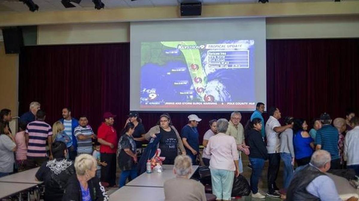 FILE: Evacuees stand in line for lunch Sept. 9, 2017, underneath a projected weather forecast at the Buffalo Creek Middle School shelter as Hurricane Irma approaches Manatee County.