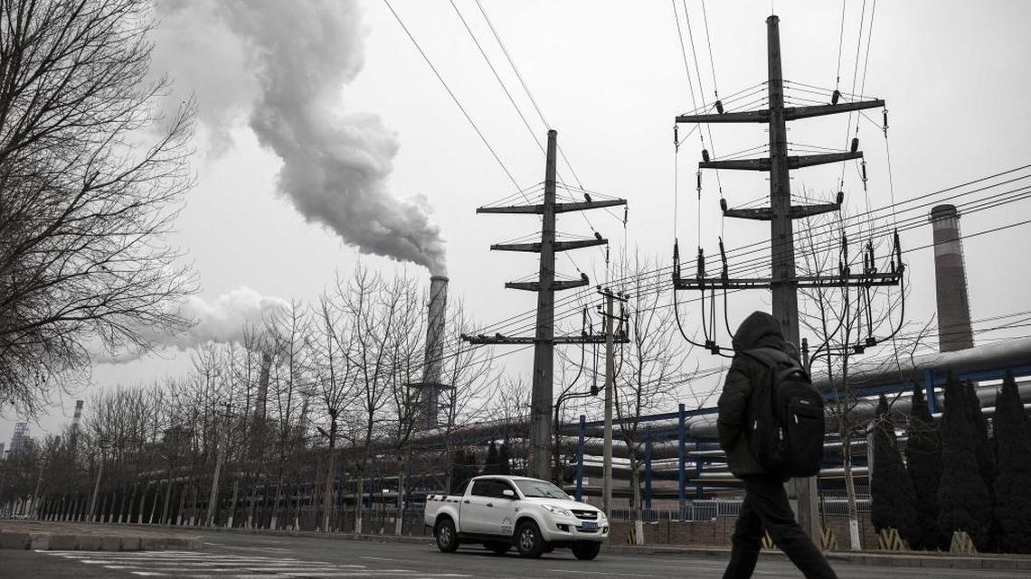 FILE: A pedestrian walks on a street as smoke billows from the chimneys of a factory in Dalian, China.