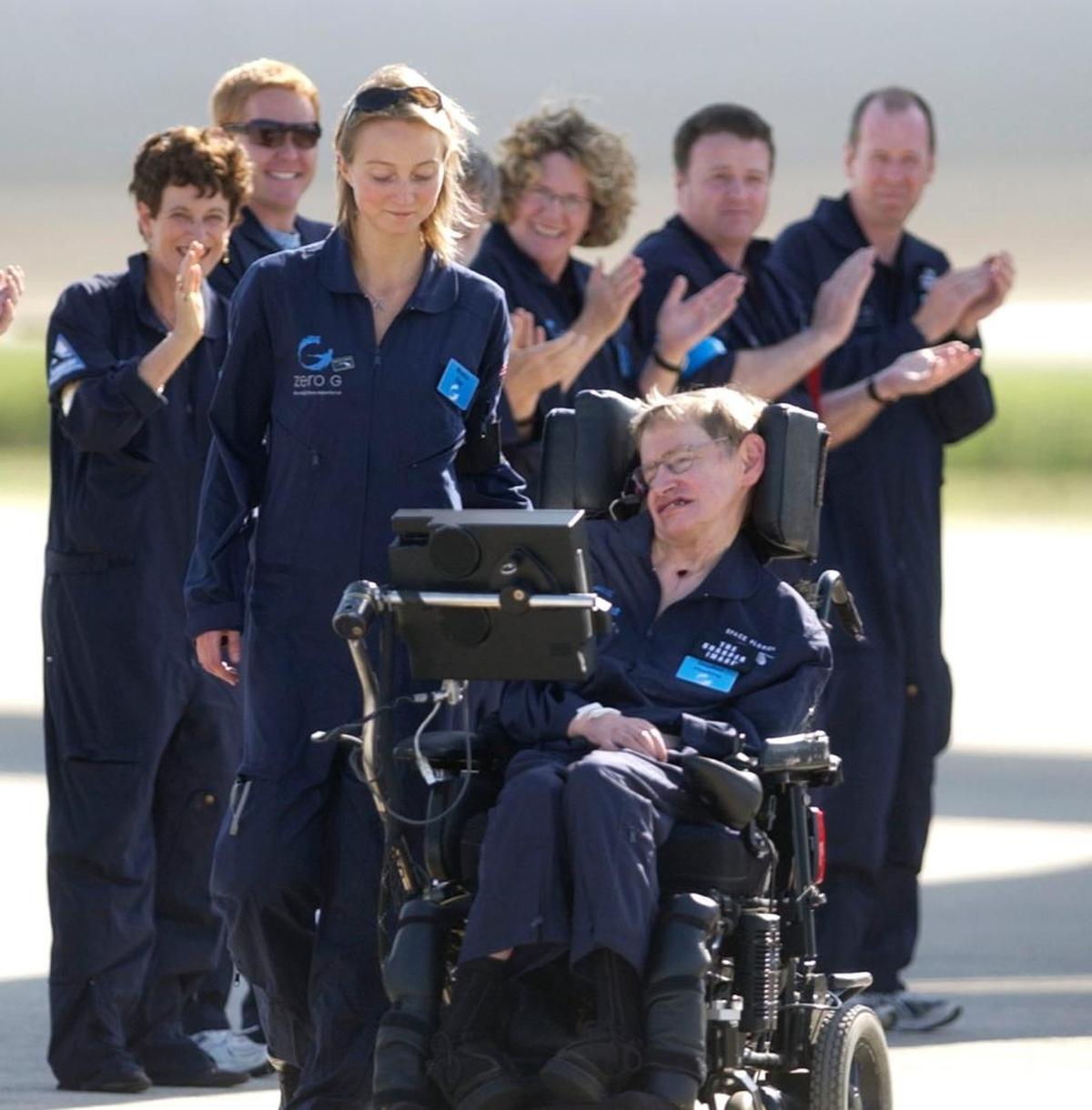 FILE - Astrophysicist Stephen Hawking is assisted off the tarmac at the Kennedy Space Center by his caregiver, Monica Guy, as he is applauded by members of the flight crew after completing a zero-gravity flight, Thursday, April 26, 2007, in Cape Canaveral, Fla.
