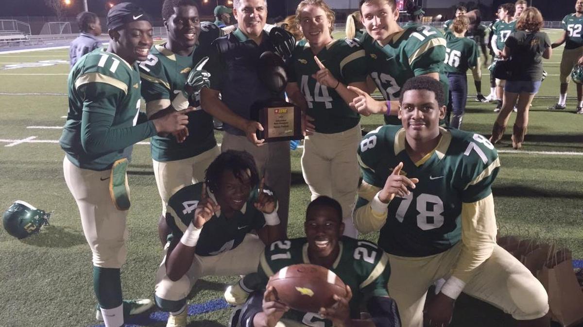 Saint Stephen’s players surround head coach Tod Creneti as he holds the Sunshine State Athletic Conference championship trophy Saturday night after the Falcons defeated Saint Edward’s in Oviedo.